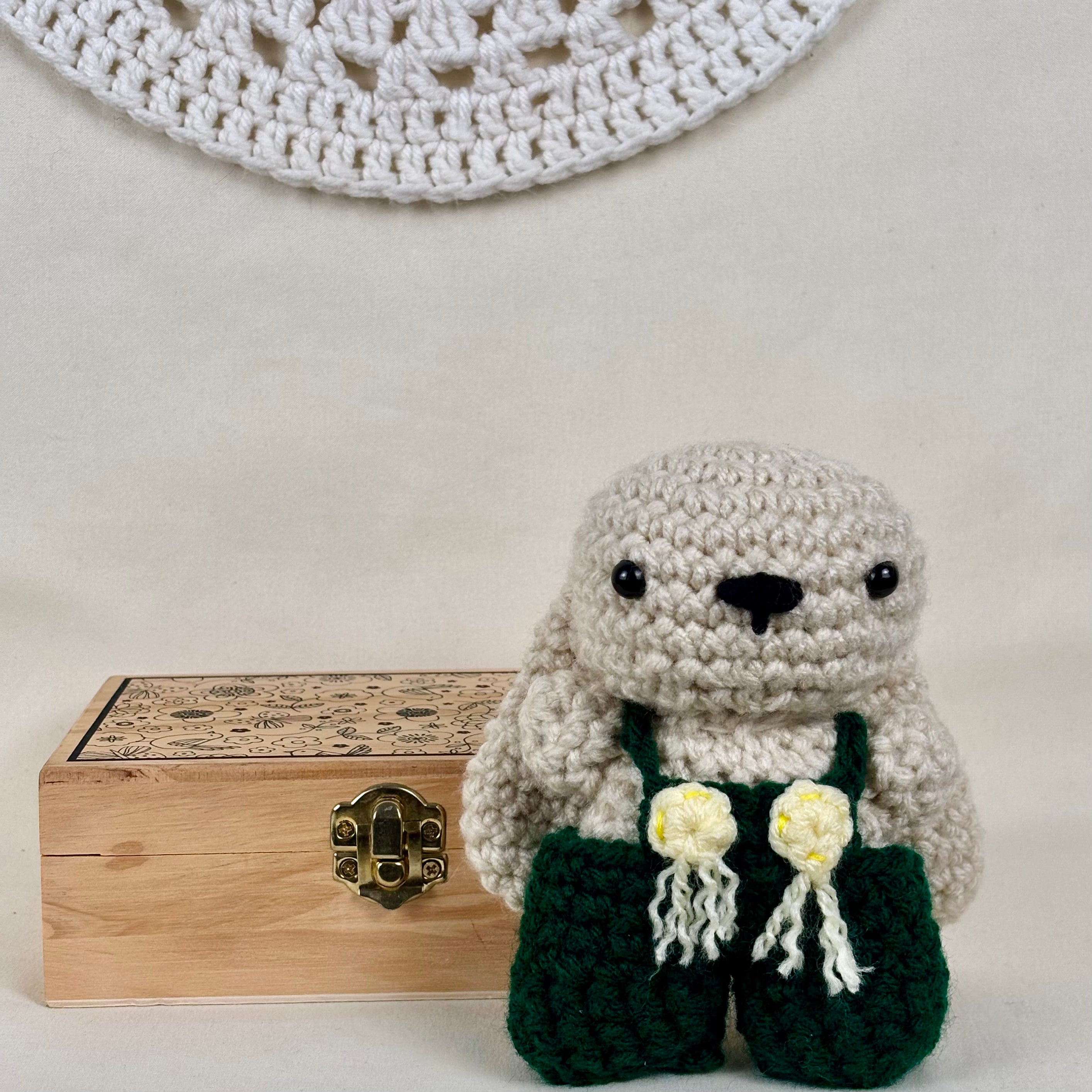 Crocheted animal toy with green overalls and wooden box on a light background